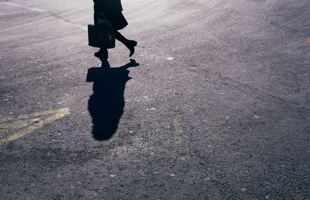 person in black coat walking on gray asphalt road during daytime